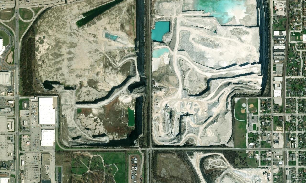 Satellite imagery of an active aggregate quarry with benches, haul roads and stockpiles.